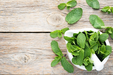 Fresh mint leafs in mortar on grey wooden table