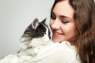 Beautiful young woman holding cat on grey background