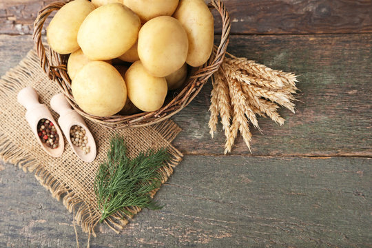 Potatoes in wicker basket with pepper and wheat ears on wooden background