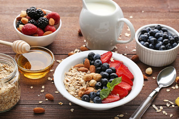 Oat flakes in plate with berries, nuts, honey and milk on wooden table