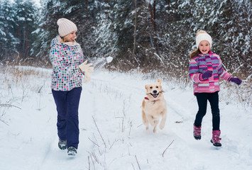 Fototapeta na wymiar Cheerful mom and her cute daughter with their dog golden retriever in winter