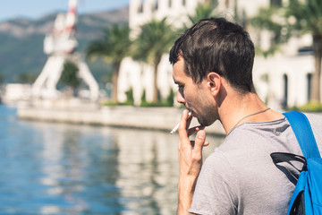 Young bearded man with cigarette outdoors in summer on sea wters on background