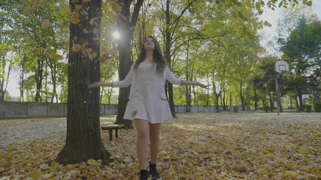Slim model girl enjoying a day in park smiling and spinning among falling autumn leaves enjoying freedom in slow motion