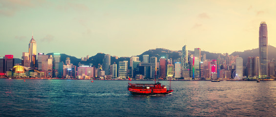 Obraz premium Spectacular skyline of Hong Kong island, China, with skyscrapers and historic boat sailing at sunset. Panoramic travel background.