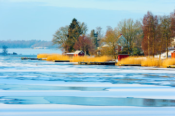 Piers in the reed beds on a winter morning. Sheds and houses visible on the peninsula. Ice cover...