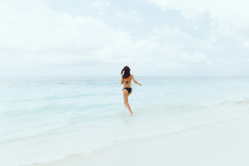 Summer background. Young woman runs into ocean