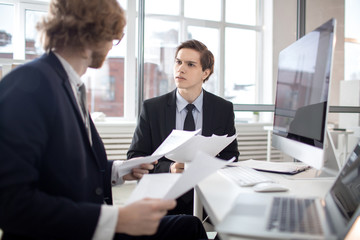 Two young bankers sitting in office and discussing papers and financial information