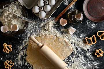 Cooking dough for cookies, butter, eggs, cooking equipment, flour on a black table. Top view with copy space, mockup for menu, recipe or culinary classes. Baking background.