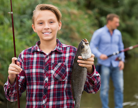Smiling teenage boy holding catch freshwater fish