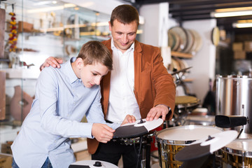 Obraz na płótnie Canvas Father and teenage son examining drum units in guitar shop