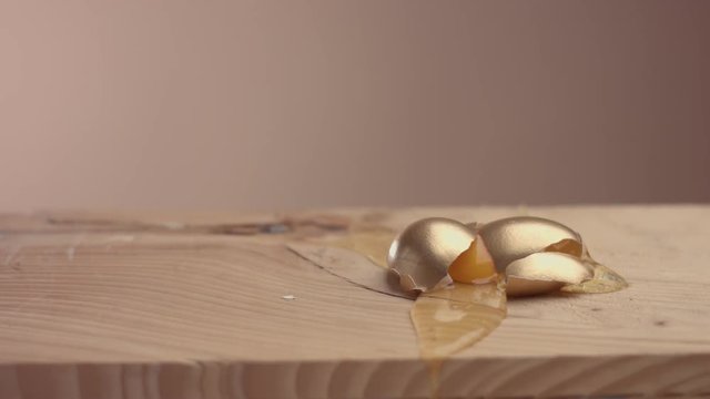slow motion how golden egg falling and broken on wooden desk