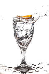 Orange splashing into glass of water with ice cubes