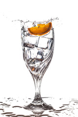 Orange slice splashing into glass of water