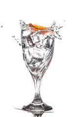 Orange slice splashing into glass of water with ice cubes