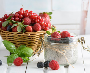Healthy blended smoothie made from almond milk. Glass jar with chia pudding with fresh strawberries, raspberries and blueberries. Basket with berries. On a wooden light background.