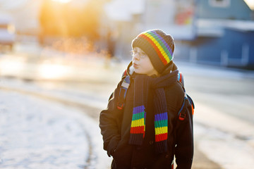 Happy kid boy with backpack or satchel having fun with snow on way to school