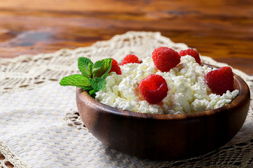 Cottage cheese with fresh raspberry in a wooden bowl on old wooden background with copy space for your text. Top view