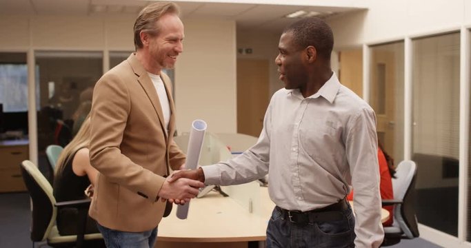 4K Smiling mixed ethnicity architects greet each other & shake hands before planning meeting. Slow motion.