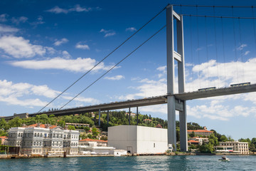 View of the First Bosporus Bridge. Ships passing through bridge connecting Europe and Asia. Sunny day with background of cloudy blue sky. Istanbul. Turkey.