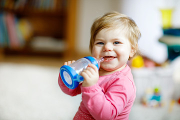 Cute adorable ewborn baby girl holding nursing bottle and drinking formula milk or water