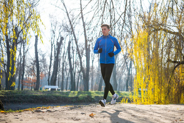 Fototapeta premium Young Sports Man Running in the Park in Cold Sunny Autumn Morning. Healthy Lifestyle and Sport Concept.