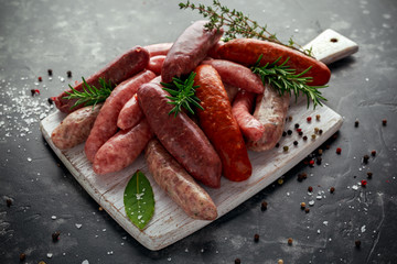 Freshly made raw breed butchers sausages mix in skins with herbs on white cutting board.