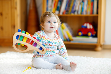 Adorable cute beautiful little baby girl playing with educational wooden music toys at home or...