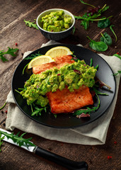 Oven cooked salmon steak, fillet with avocado salsa and green on black plate. wooden table. healthy food