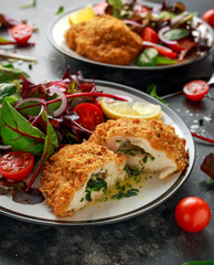 Breaded Chicken Kiev breast stuffed with butter, garlic and herbs served with vegetables in a plate.
