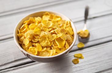 Bowl with cornflakes on white wooden background