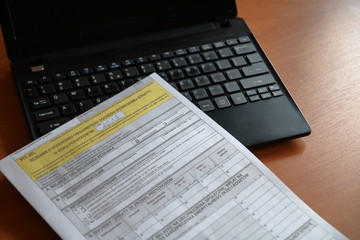 Formularz podatkowy, polski, leży na czarnym otwartym laptopie, na brązowym biurku