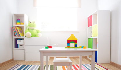 Colourful children rooom with white walls and furniture. Rainbow carpet at home interior with a...