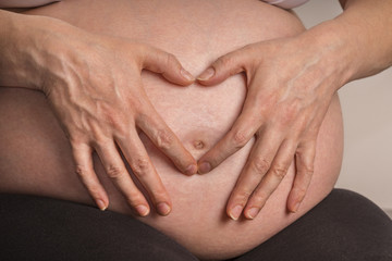 Hände formrn Herz auf Babybauch einer hoch Schwangeren