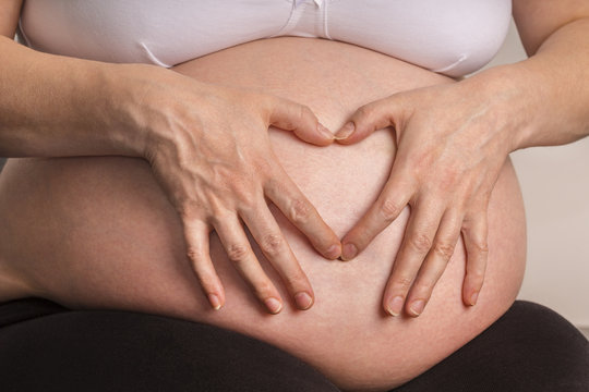 Hände formrn Herz auf Babybauch einer hoch Schwangeren