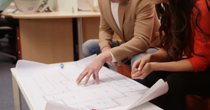 4K 2 Architects discussing building plans in the office with staff working in the background. Slow motion.