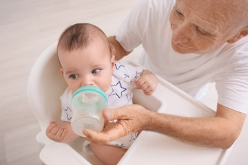 Senior man giving drink to his little grandchild at home