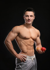 Fototapeta na wymiar Handsome muscular young man with apples on black background