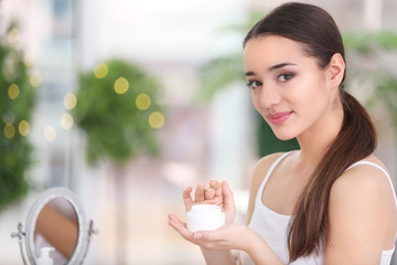 Young woman with jar of hand cream indoors