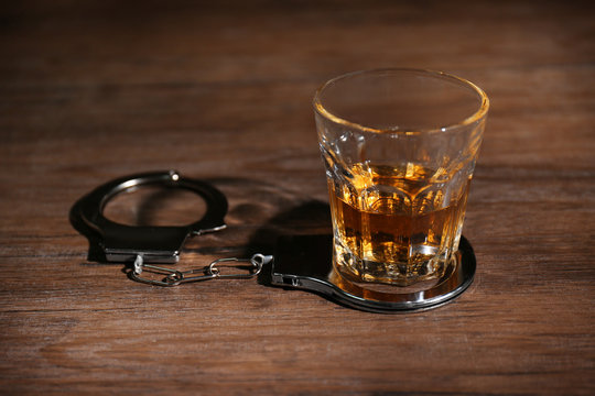 Glass of alcohol and handcuffs on table
