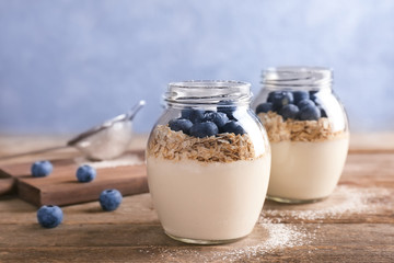 Yogurt with oat flakes and blueberry in jars on wooden table