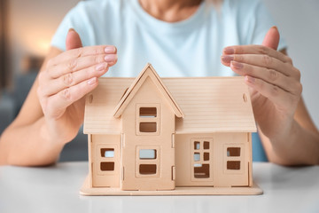 Woman protecting house model on table, closeup