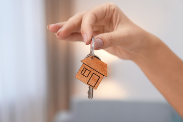 Woman holding house key on blurred background, closeup