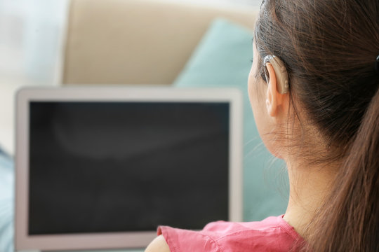 Young woman with hearing aid using laptop indoors