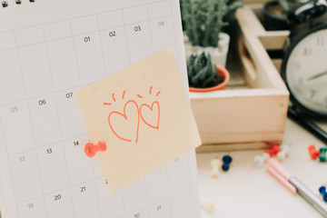post note paper with couple heart sticky on calendar and business equipment clock, plant background. image for copy space, business, office, celebration concept