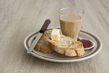 MILK COFFEE ON WOOD TABLE
Two brown crusty sliced french toasts are served in a plate with butter,...