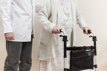 10.	Pielęgniarz pomaga iść starej kobiecie trzymającej się chodzika. - obrazy, fototapety, plakaty