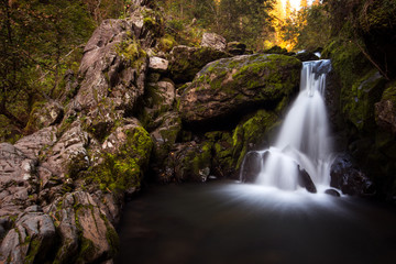 Fototapeta na wymiar Beautiful fairy mountain waterfall in a fairy forest among rocks at sunset