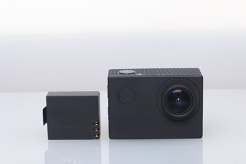 The action camera lies on a white surface. Near the spare battery.