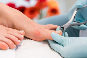 Close-up of the hands of a pedicurist wearing sterile surgical gloves, while using a toe nail clipper while shaping the nails of a female customer in a beauty salon