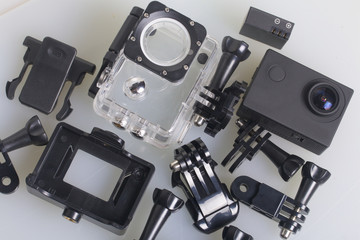 The action camera lies on a white surface. The action camera lies on a white surface. Near the box for underwater shooting, spare battery and other accessories. View from above.